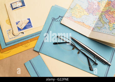 Envelopes with stamps, pen, glasses, notebook with a map are on the surface. Stock Photo