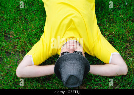 man in yellow T-shirt and hat lying on green grass at park Stock Photo