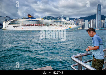 HONG KONG, VICTORIA HARBOUR: A man is handline fishing at the side of Victoria Harbour while a luxury cruise liner passes by. Stock Photo