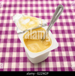 Open yogurt in pot with metal spoon closeup Stock Photo