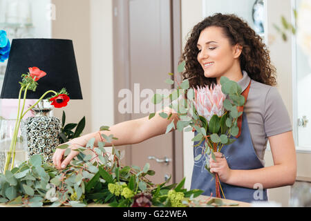 Happy attractive young woman florist making bouquet on the table in shop Stock Photo