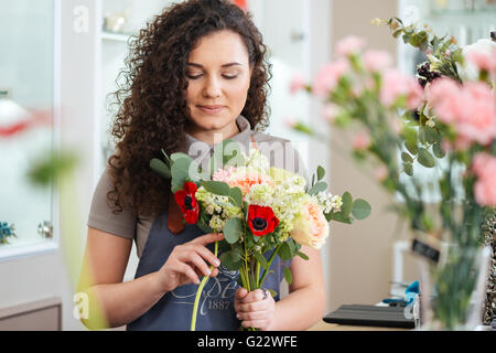 Thoughtful cute young woman florist holding flowers and making bouquet in shop Stock Photo
