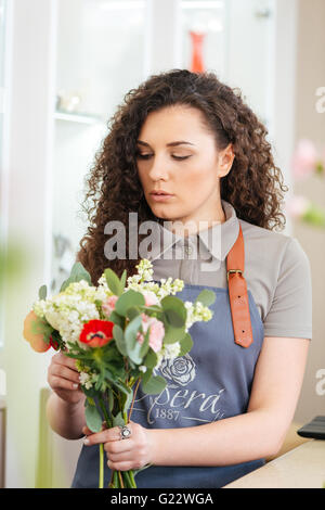 Attractive focused young woman florist in apron working and  making flower bouquet in shop Stock Photo