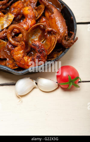 fresh seafood stew prepared on an iron skillet ove white rustic wood table Stock Photo