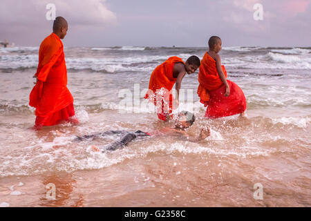 Colombo, Sri Lanka,   23rd May, 2016. Young novice monks and others play in the sea at sunset at Galle Face Green. It is a public holiday, and day three  of Vesak celebrations, which commemorates the birth of Buddha, his attaining enlightenment and his passing away on the full moon day of May which fell this year on May 21. Colombo, Sri Lanka. Stock Photo