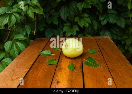 yellow apple and waterdrops on a wooden table and fallen autumn leaves Stock Photo