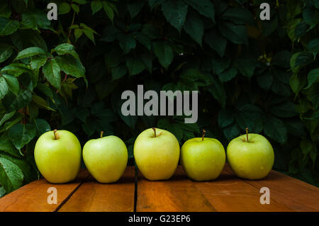 A few yellow apples and waterdrops on a wooden table and fallen autumn leaves Stock Photo