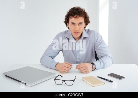 Serious young businessman sitting at his workplace and looking at camera Stock Photo