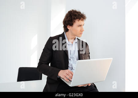 Pensive businessman leaning on the table with laptop computer and looking away Stock Photo