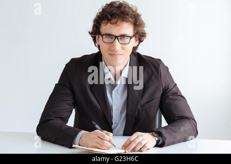 Businessman writing something in notebook and looking at camera in office Stock Photo