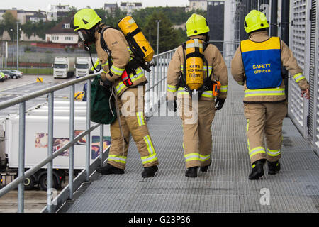 Firefighters wearing breathing apparatus prepare to throw a line from an external access platform during a simulated chemical incident at an industrial premises. Stock Photo