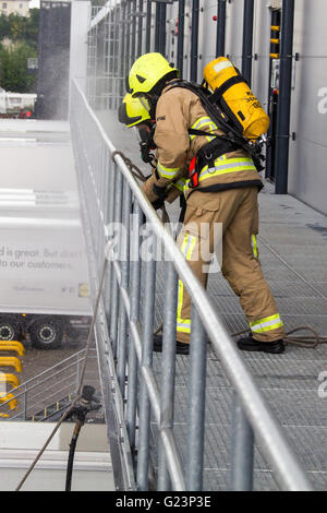 Firefighter wearing breathing apparatus drags a hosereel line on a gantry access platform during a simulated chemical incident at an industrial premises. Stock Photo