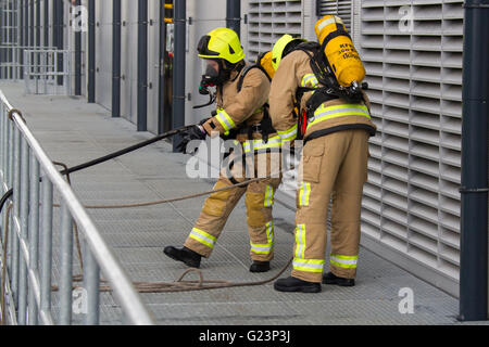 Firefighter wearing breathing apparatus drags a hosereel line on a gantry access platform during a simulated chemical incident at an industrial premises. Stock Photo