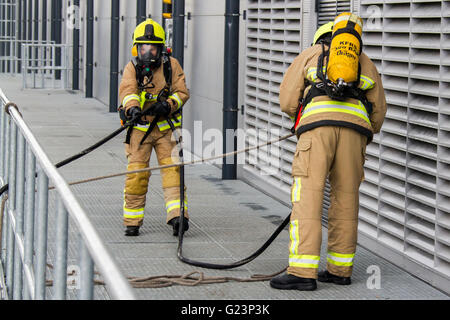 Firefighter wearing breathing apparatus drags a hosereel line on a gantry access platform during a simulated chemical incident at an industrial premises. Stock Photo