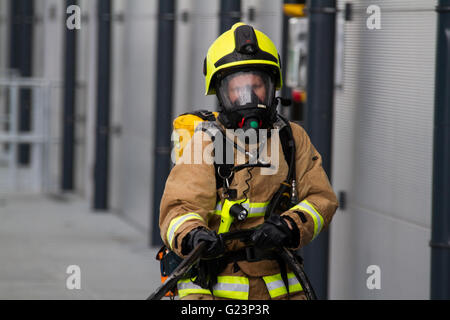 Female Firefighter wearing breathing apparatus drags a hosereel line on a gantry access platform during a simulated chemical incident at an industrial premises. Stock Photo