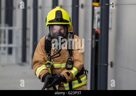 Female Firefighter wearing breathing apparatus drags a hosereel line on a gantry access platform during a simulated chemical incident at an industrial premises. Stock Photo