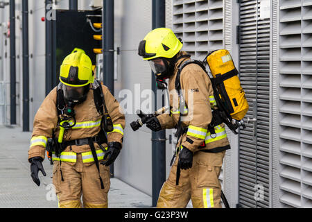 Firefighter wearing breathing apparatus drags a hosereel line on a gantry access platform during a simulated chemical incident at an industrial premises. Stock Photo