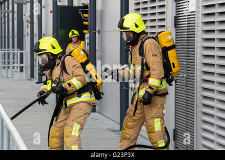 Firefighter wearing breathing apparatus drags a hosereel line on a gantry access platform during a simulated chemical incident at an industrial premises. Stock Photo