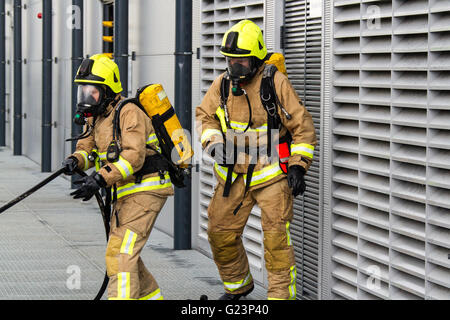 Firefighter wearing breathing apparatus drags a hosereel line on a gantry access platform during a simulated chemical incident at an industrial premises. Stock Photo