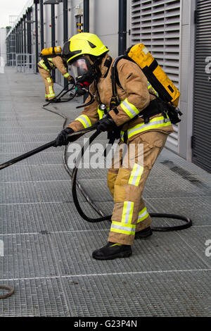 Firefighter wearing breathing apparatus drags a hosereel line on a gantry access platform during a simulated chemical incident at an industrial premises. Stock Photo