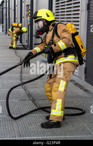 Firefighter wearing breathing apparatus drags a hosereel line on a gantry access platform during a simulated chemical incident at an industrial premises. Stock Photo