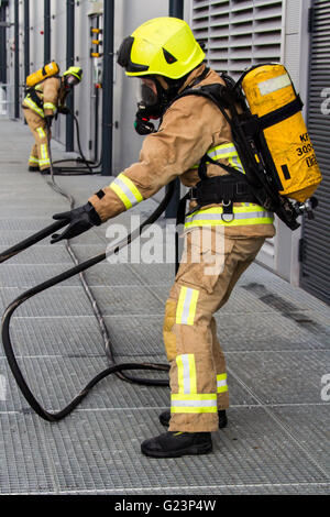 Firefighter wearing breathing apparatus drags a hosereel line on a gantry access platform during a simulated chemical incident at an industrial premises. Stock Photo