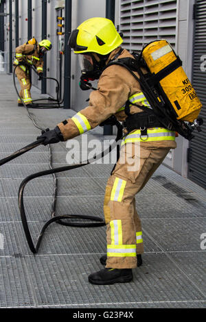 Firefighter wearing breathing apparatus drags a hosereel line on a gantry access platform during a simulated chemical incident at an industrial premises. Stock Photo