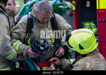 Firefighters assist a colleague don a gas tight suit. Stock Photo