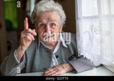 An elderly woman sitting at a table and specifies the finger. Stock Photo