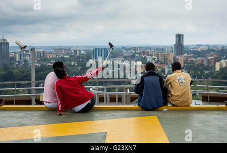 Four teenagers take a selfie with a selfie stick, atop the KICC building looking out over the city in Nairobi, Kenya, while on CCTV Stock Photo