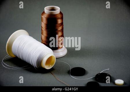 Brown thread with white thread.And buttons black and white.On black background.story of fashion or garment business or clothes. Stock Photo