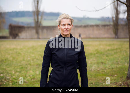 A medium shot of a middle aged female jogger standing in a park. Stock Photo
