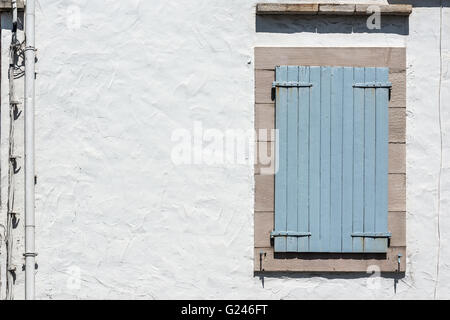 Blue wooden window panel with a rusty metal hinges on a white wall. Stock Photo