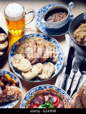 Czech national cuisine, salad made with sausages, roast pork with sauerkraut and dumplings, pancakes, beer Stock Photo