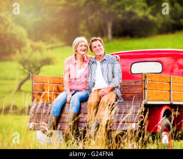 Senior couple sitting in back of red pickup truck Stock Photo