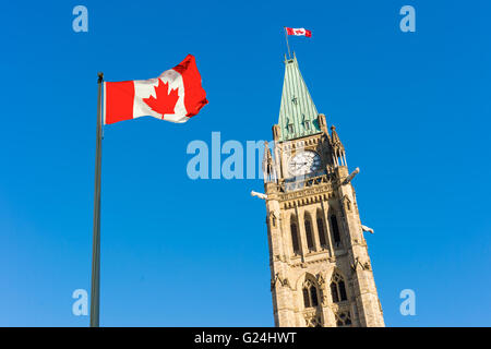 Peace Tower of Canadian Parliament Building with a big canadian flag over blue sky in Ottawa, Canada Stock Photo