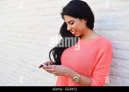 Young beautiful latin woman texting on her phone. Woman using a cellphone wearing casual clothes. Stock Photo