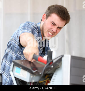 Portrait of furious and crazy man without self control hitting a computer with a hammer hating technology problems in office Stock Photo