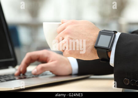 Close up of an executive working on line with laptop and a modern generic smart watch while drinks hot beverage in a restaurant Stock Photo