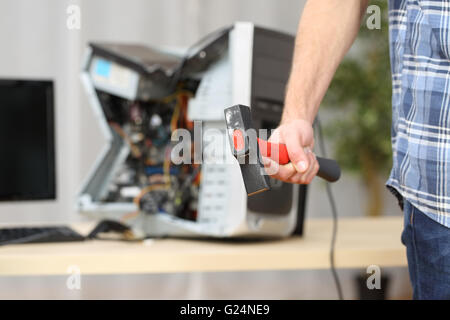 Hand of a furious hot-tempered man holding a hammer after destroying a computer on a table Stock Photo