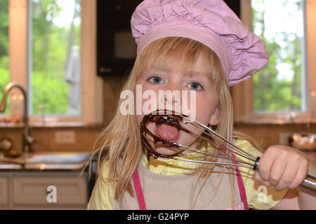 young girl licking batter of whisk Stock Photo