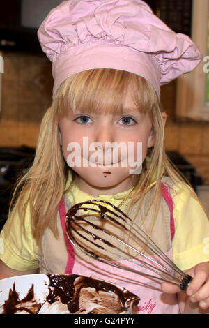 young girl licking batter of whisk Stock Photo