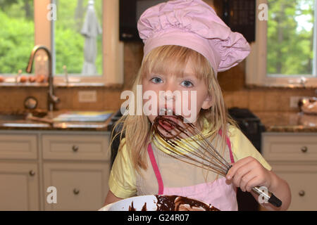 young girl licking batter of whisk Stock Photo