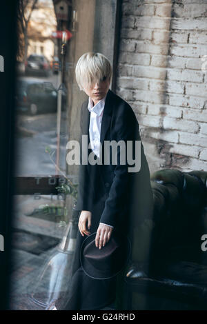 Cute blonde girl looking confused in modern cafe and looking at something Stock Photo