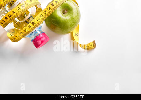 Measuring tape around a bottle of mineral water and apple on white table. Concept health, diet and nutrition. Stock Photo
