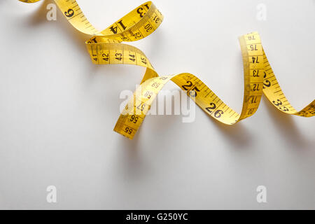 Yellow tape measure in meters and inches in a spiral on white table. Top view. Horizontal composition. Stock Photo