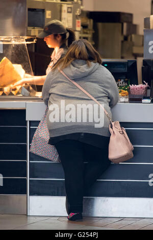 Obese overweight woman ordering fast food in a take away restaurant. Stock Photo