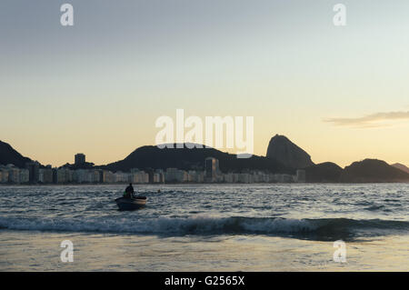 Brazilian fishermen launch a brightly painted fishing boat on a tranquil morning on Copacabana Beach. Stock Photo