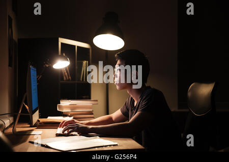 Serious asian young man using computer and typing in dark room Stock Photo