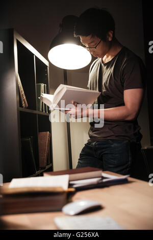 Attractive asian young man in glasses standing and reading book in the evening Stock Photo